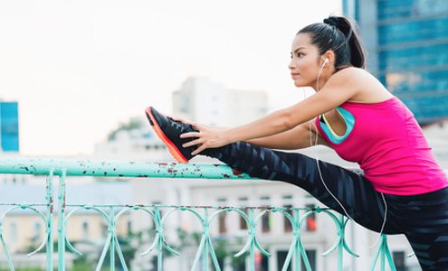 A lady wearing her fitness clothing stretching on a hand rail. The lady is also wearing earphones.