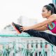A lady wearing her fitness clothing stretching on a hand rail. The lady is also wearing earphones.