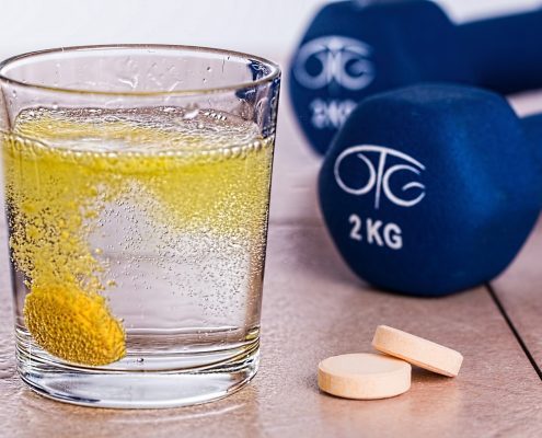 An effervescent tablet dispersing in a glass of water set in front of 2kg dumbbells